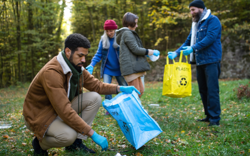 A group of people on their eco journey is picking up litter in a wooded area. They are holding recycling bags, wearing gloves, and demonstrating climate action with personal priorities focused on a cleaner environment.