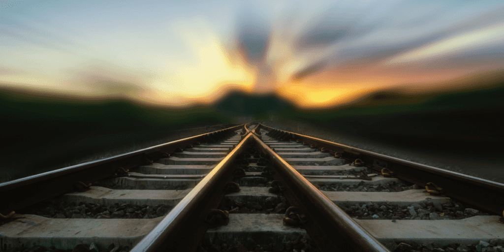 A set of blurred railway tracks stretch into the vibrant sunset, where colorful skies and clouds paint a vision of hope and progress.