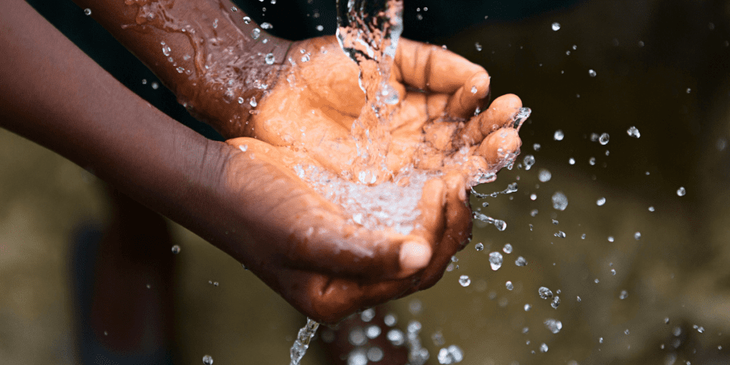 Hands cupped together catching splashing water droplets, a simple yet profound act in low-income nations where access to clean water is often threatened by invisible chains of poverty.