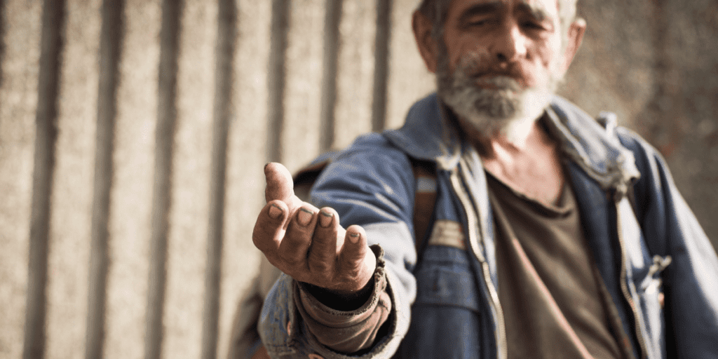 An elderly man stands against a concrete wall, his outstretched hand symbolizing the invisible chains of poverty.