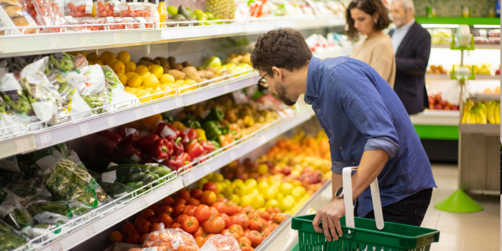 At a supermarket produce section, a man carefully shops for vegetables.