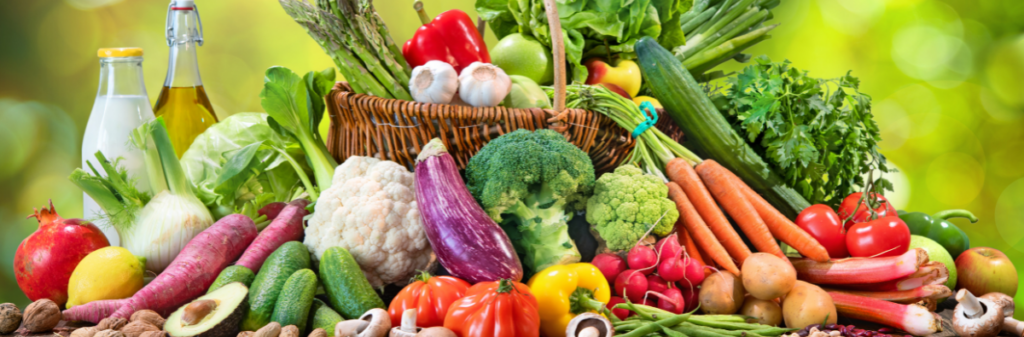 Assorted fresh vegetables and organic fruits are arranged around a basket on a vibrant green background.