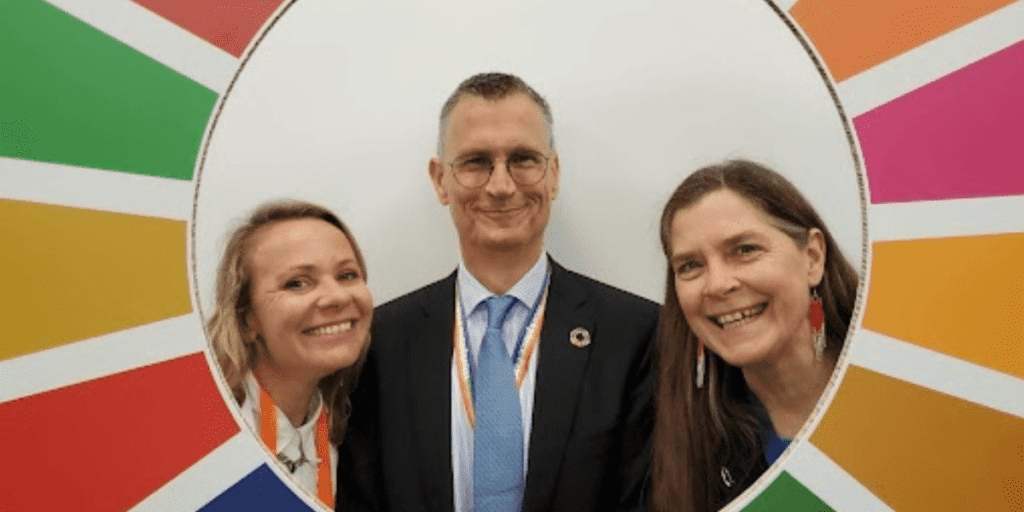 Three people smiling in front of a colorful circular backdrop, capturing the spirit of sustainability in vibrant Frankfurt.