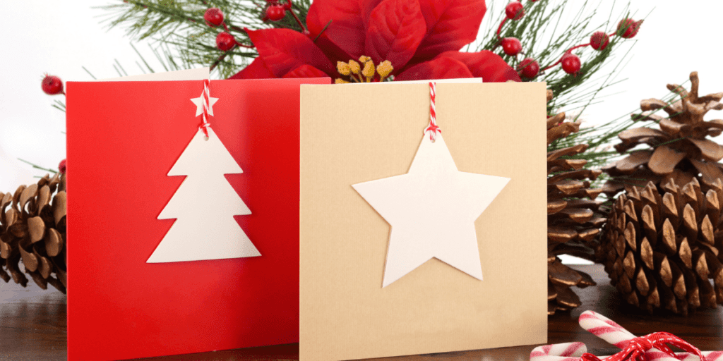 Two holiday cards: one red with a tree, one beige with a star, and pine cones in the background. Perfect for conscious gifting, these cards embody giving with heart, adding a personal and thoughtful touch to your holiday greetings.