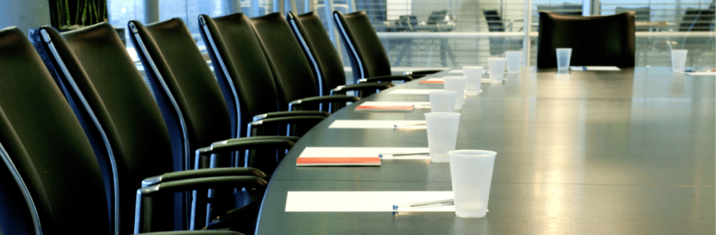 The empty conference table, prepared for an interview, is set with chairs, papers, pens, and cups.