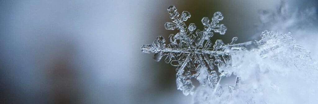 Close-up of a single snowflake with intricate details, capturing the beauty of frozen light against a blurred icy background.