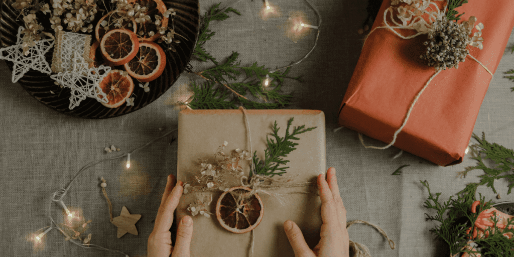 Thoughtful gifts wrapped in natural materials with dried orange slices and twine sit elegantly on a table, embodying the spirit of conscious gifting.
