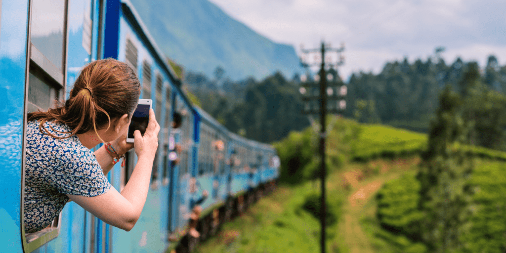A person captures the moment from a blue train, lush green hills rolling by, reminding us that thoughtful giving enhances life's beautiful journey.