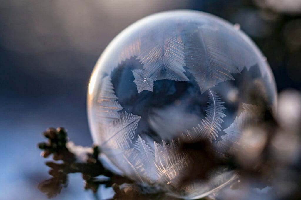 A close-up captures the beauty of a frozen soap bubble, its intricate ice flakes shimmering with a touch of frozen light against a softly blurred background.