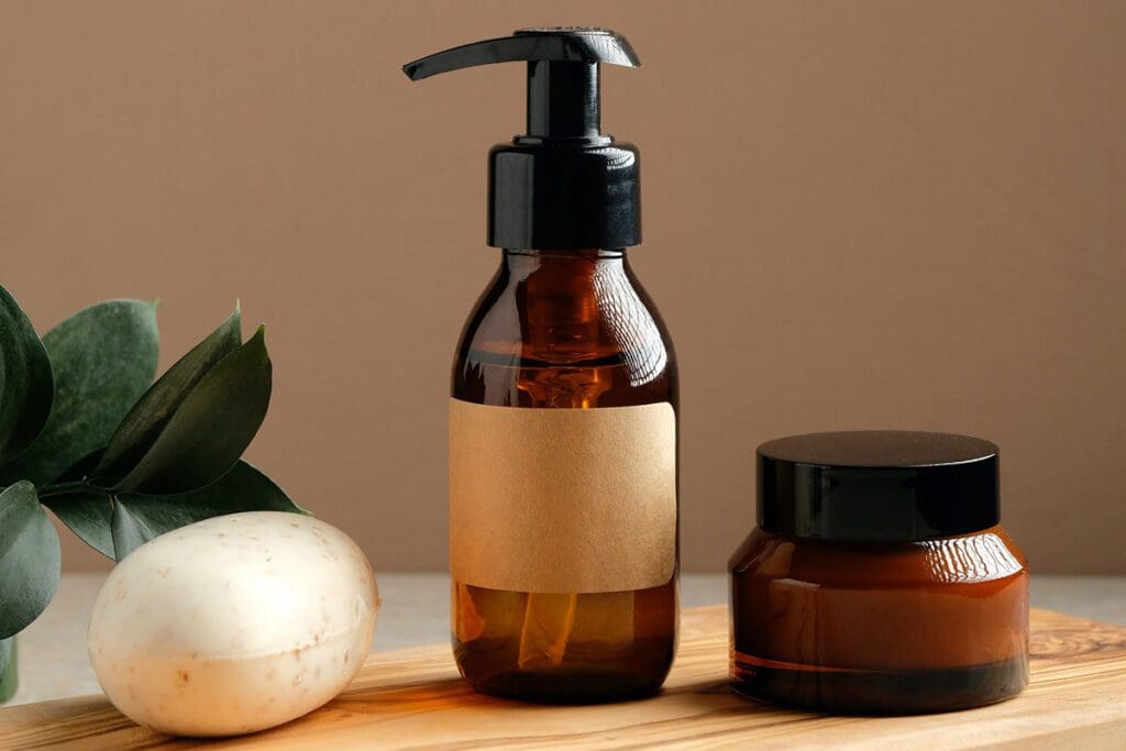 Soap, handmade lotion pump, and jar rest on a wooden surface adorned with green leaves, creating a serene holiday display.