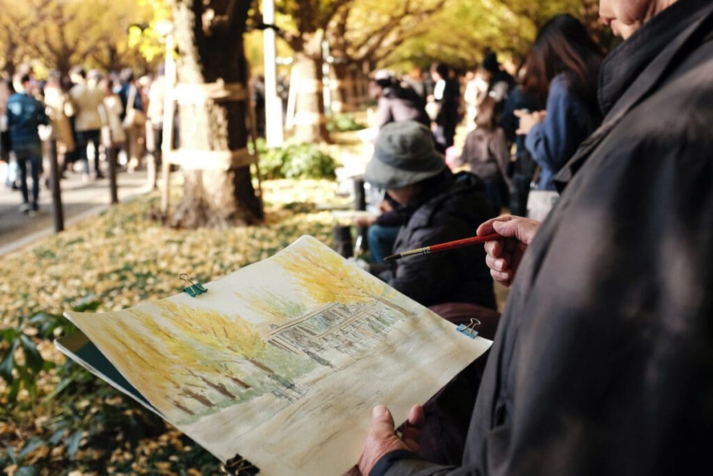An artist captures a scenic view of a tree-lined path in the Forever Forest, with people leisurely strolling in the background.