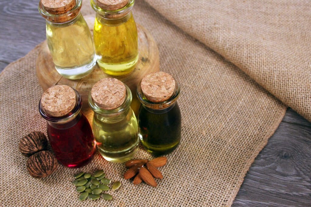 Assorted handmade bottles of oil with corks rest on burlap, surrounded by nuts and seeds, perfect for a holiday display.