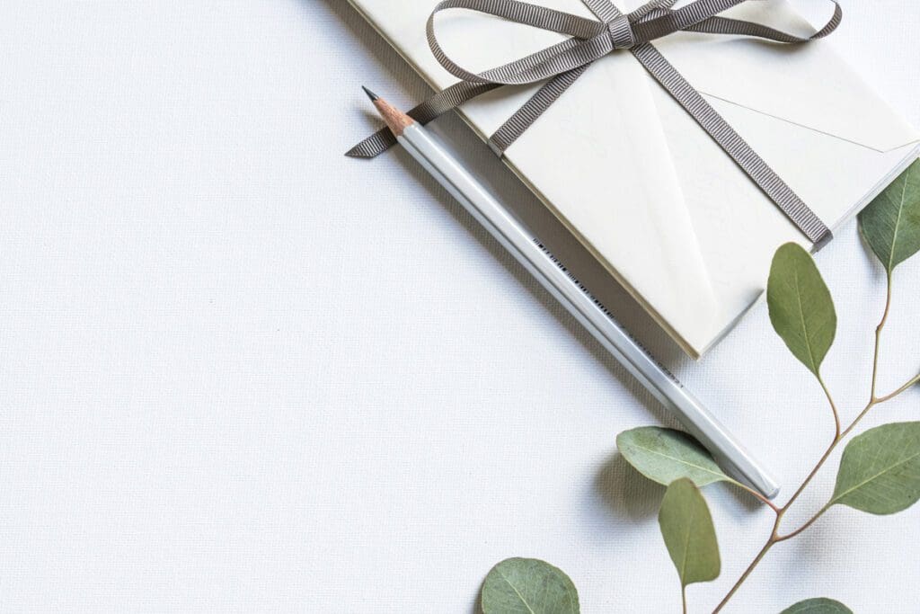 A gift with a ribbon, pencil, and eucalyptus leaves sits elegantly on a white surface—a gentle nod to the Forever Forest's commitment to planting and preserving nature's beauty.