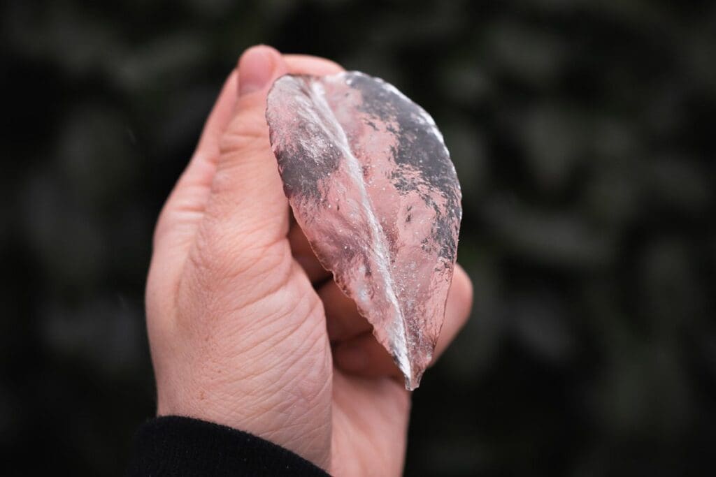 A hand elegantly holds a transparent, leaf-shaped piece of frozen light against a dark background, capturing the beauty of nature's artistry.
