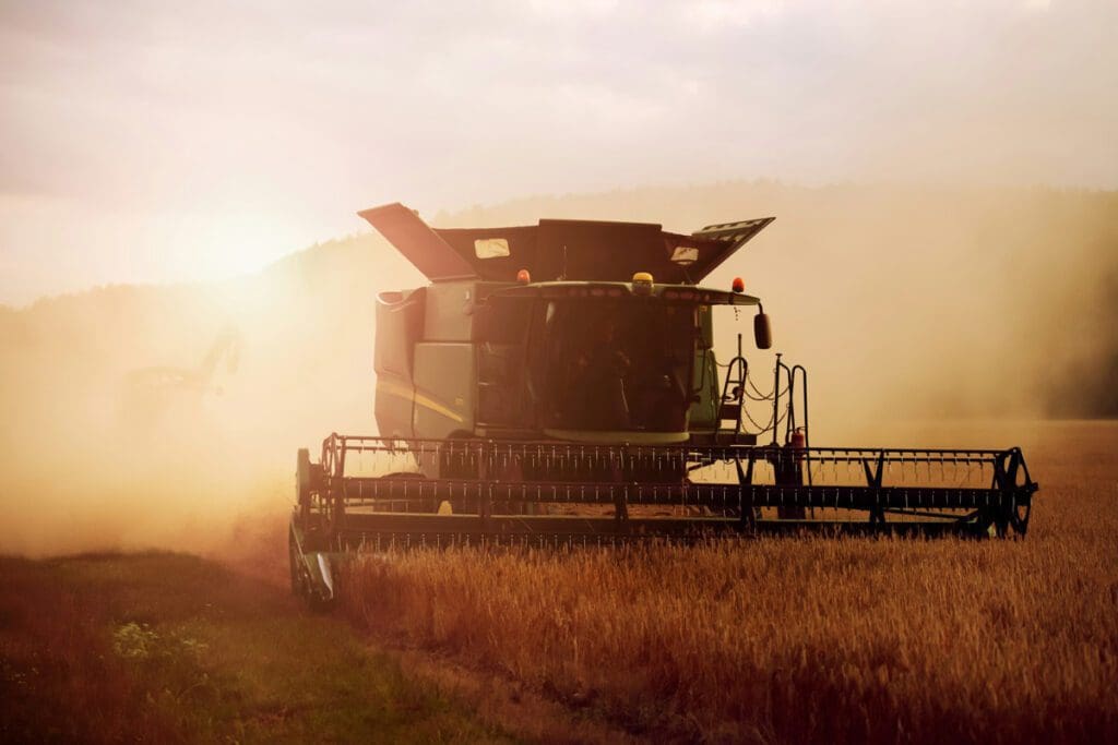 A combine harvester diligently works in a dusty field at sunset, playing its part in sustaining our planet's food system.