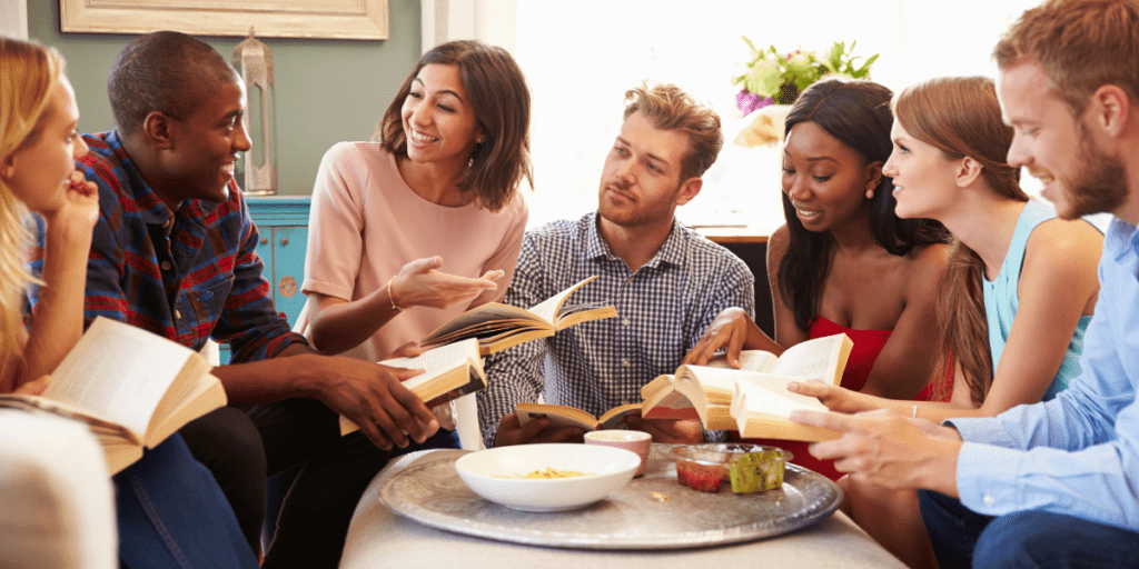 A diverse group of people sit in a circle, discussing books and enjoying snacks.