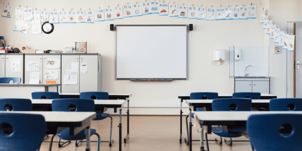 Classroom ready for schooling: blue chairs, desks, a whiteboard, and alphabet posters.