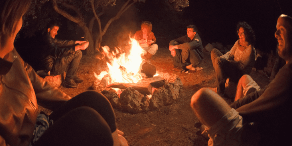 People enjoying modern communal living around a campfire, smiling and talking under the stars.