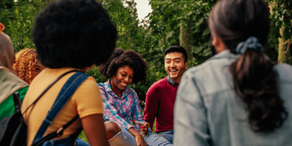 A group of people enjoying modern communal living, smiling and chatting amidst green trees.