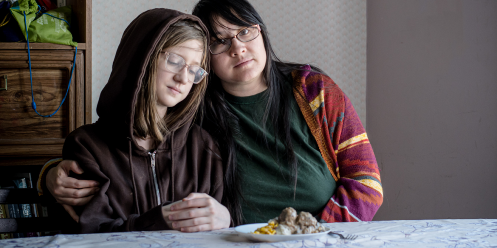 Mother and daughter sit together at a table, sharing one meal of meatballs.