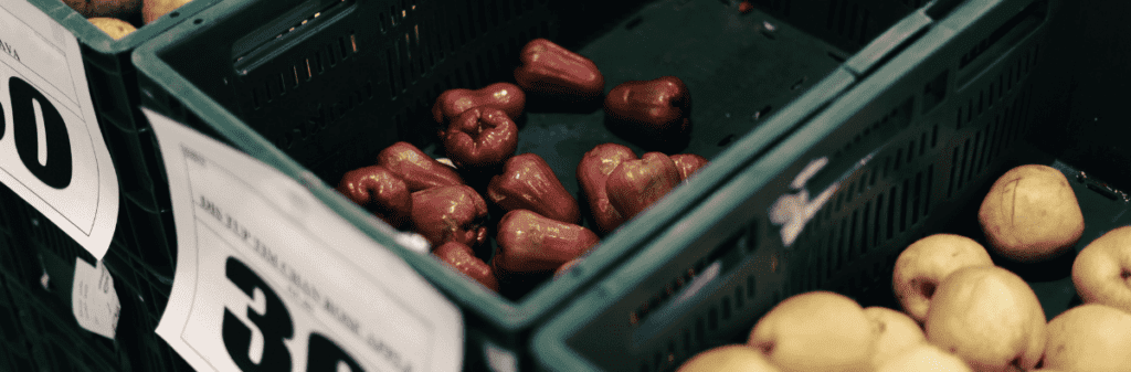 Green crates with few red bell peppers and potatoes, addressing food security at the market.