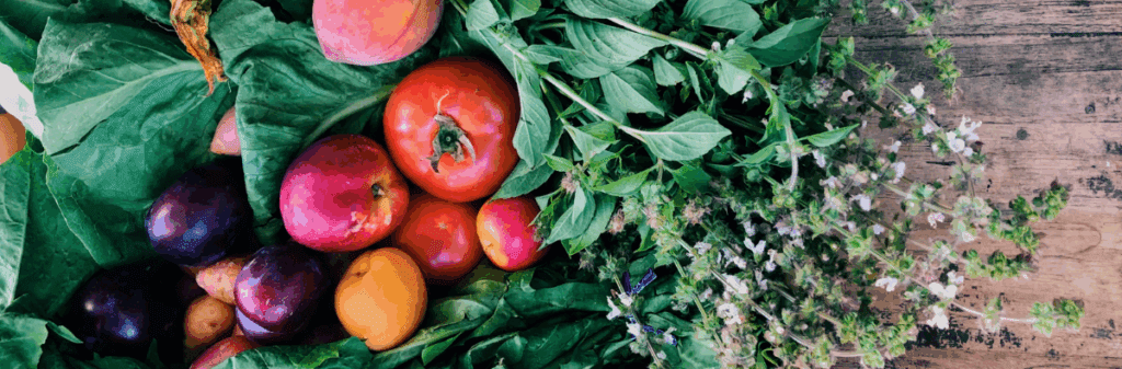 Fresh fruits and leafy greens arranged for good food on a rustic wooden surface.