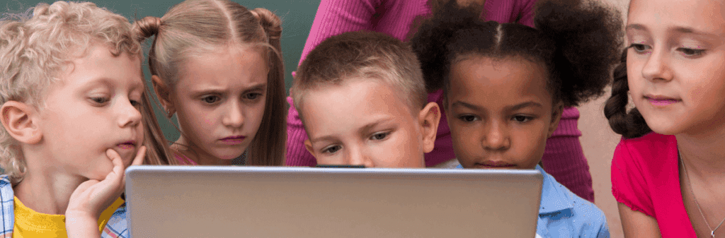 Five children in school closely looking at a laptop screen with curious and focused expressions.