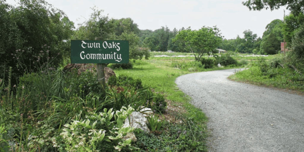 Gravel road with a "Twin Oaks Community" sign, greenery, and year-round food storage nearby.