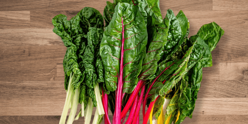 Hardy greens like rainbow chard with colorful stems on a rustic garden table.