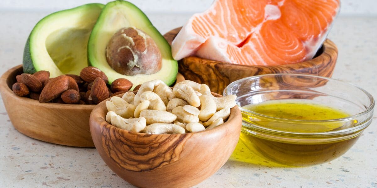 Bowls of nuts, avocado halves, salmon steak, and grains on a kitchen counter.