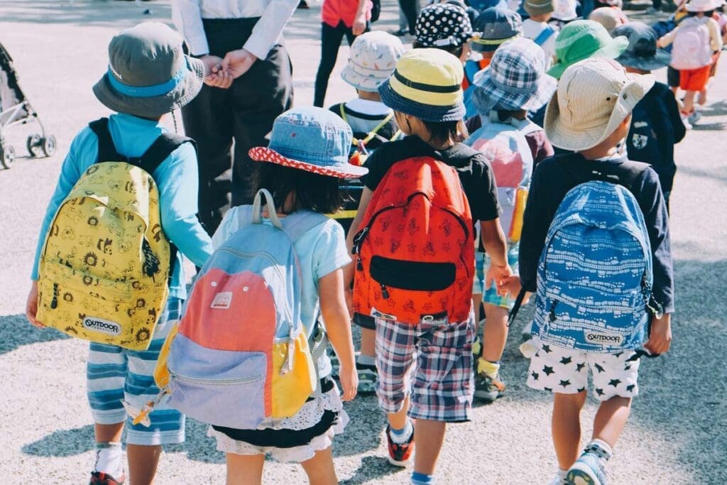 Children in hats and colorful backpacks walk together, just like in When Kids Rule the School.
