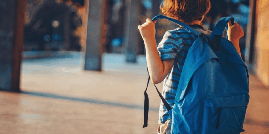 Back to school, child wearing a blue backpack outdoors, radiating summer joy on a sunny day.
