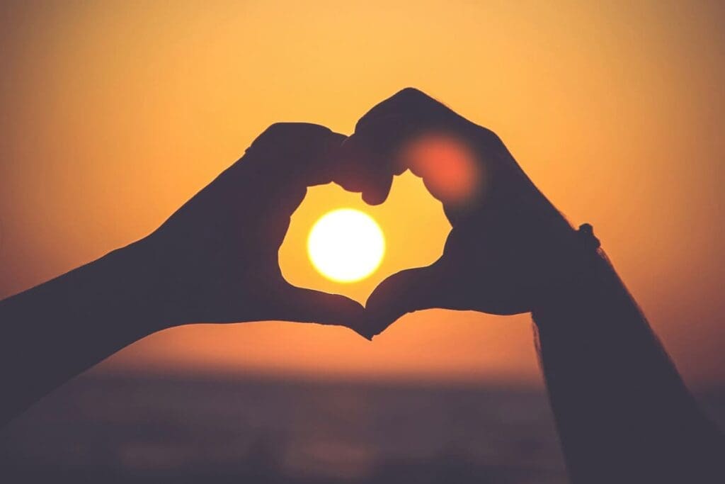Hands forming a heart around the sun at sunset, symbolizing hope in a warming world.