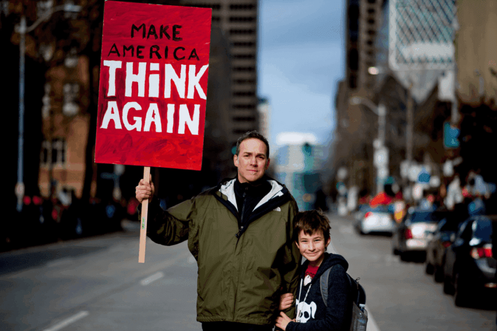 Man holding "Make America Think Again" sign, standing with child, urging climate change action.