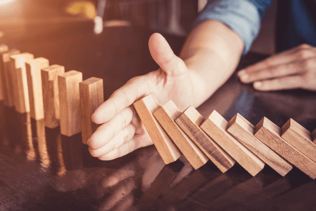 A hand stops falling dominoes—an imperfect solution in a warming world.