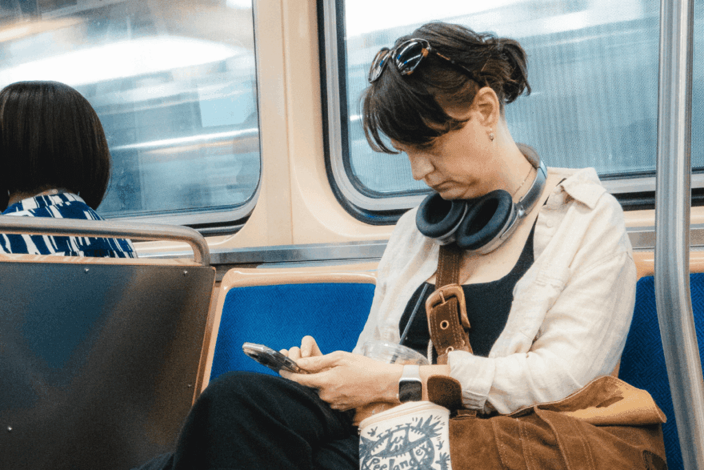 Woman with headphones sits on train, considering climate change while looking at her phone.