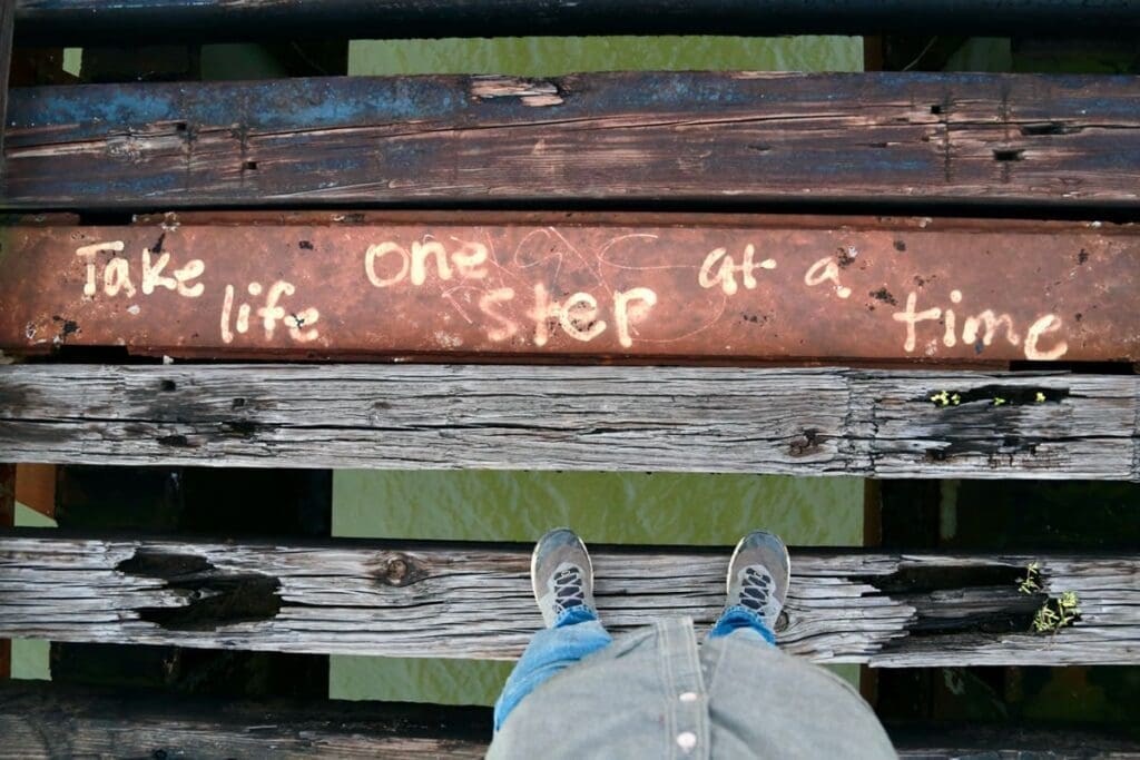 Person standing on wooden planks above water; text: "Take life one step at a time in 2025.