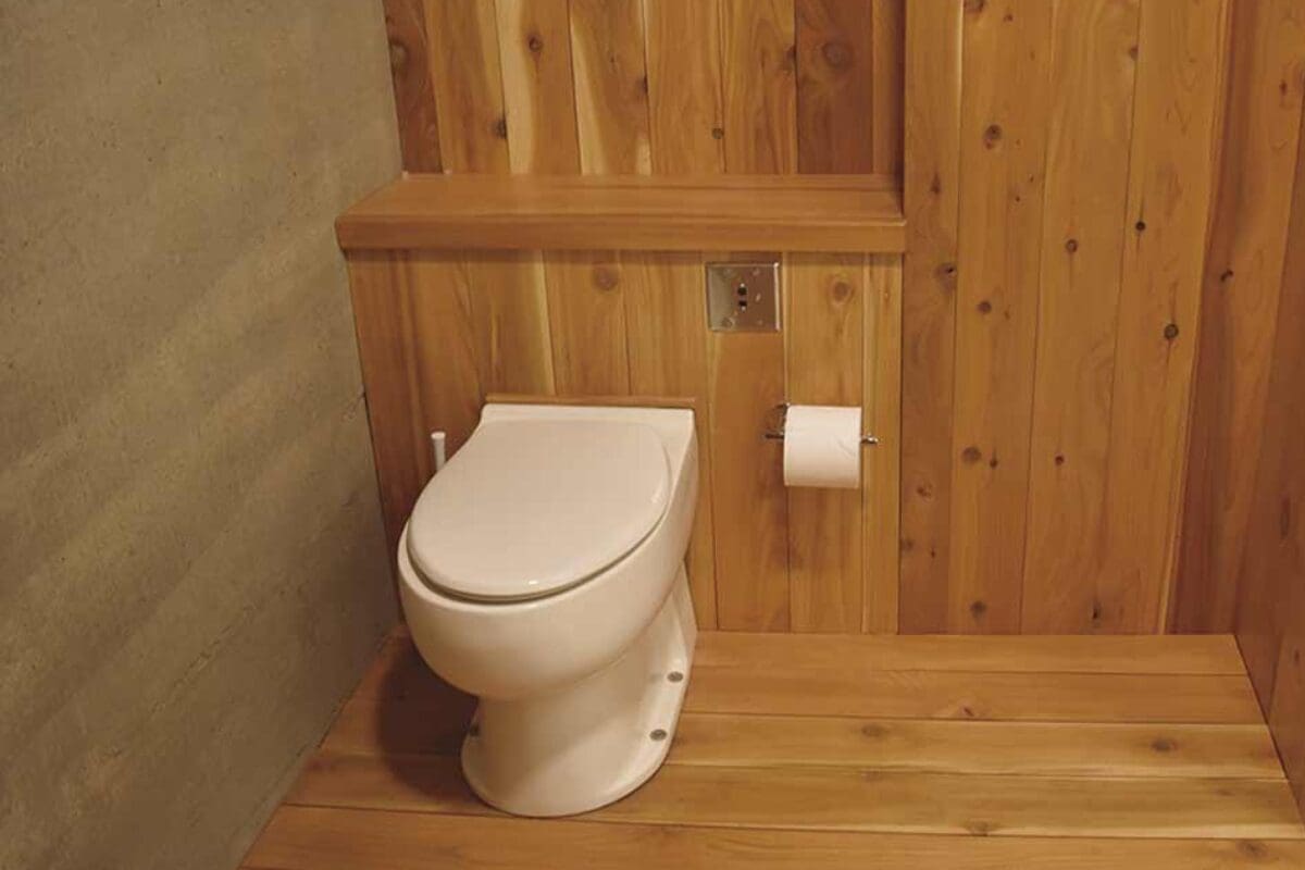 White composting toilet and toilet paper in a wooden-paneled bathroom with a concrete wall.